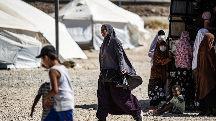 A woman walks past others gathering by the back of a pickup truck at Camp Roj, housing family members of people accused to belong to the Islamic State (IS) group who were relocated from al-Hol camp, in the countryside near al-Malikiyah (Derik) in Syria's northeastern Hasakah province on September 30, 2020. (Photo by Delil SOULEIMAN / AFP) (Photo by DELIL SOULEIMAN/AFP via Getty Images)