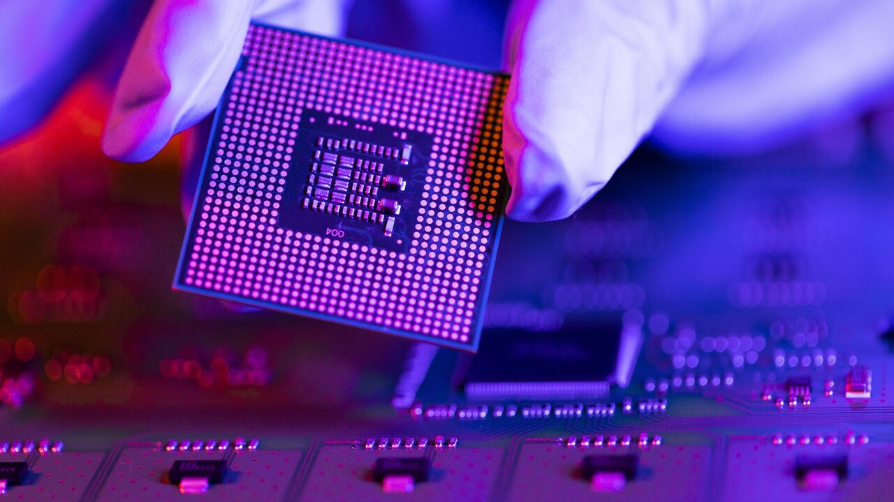 An engineer holds a CPU chip against the background of a motherboard.