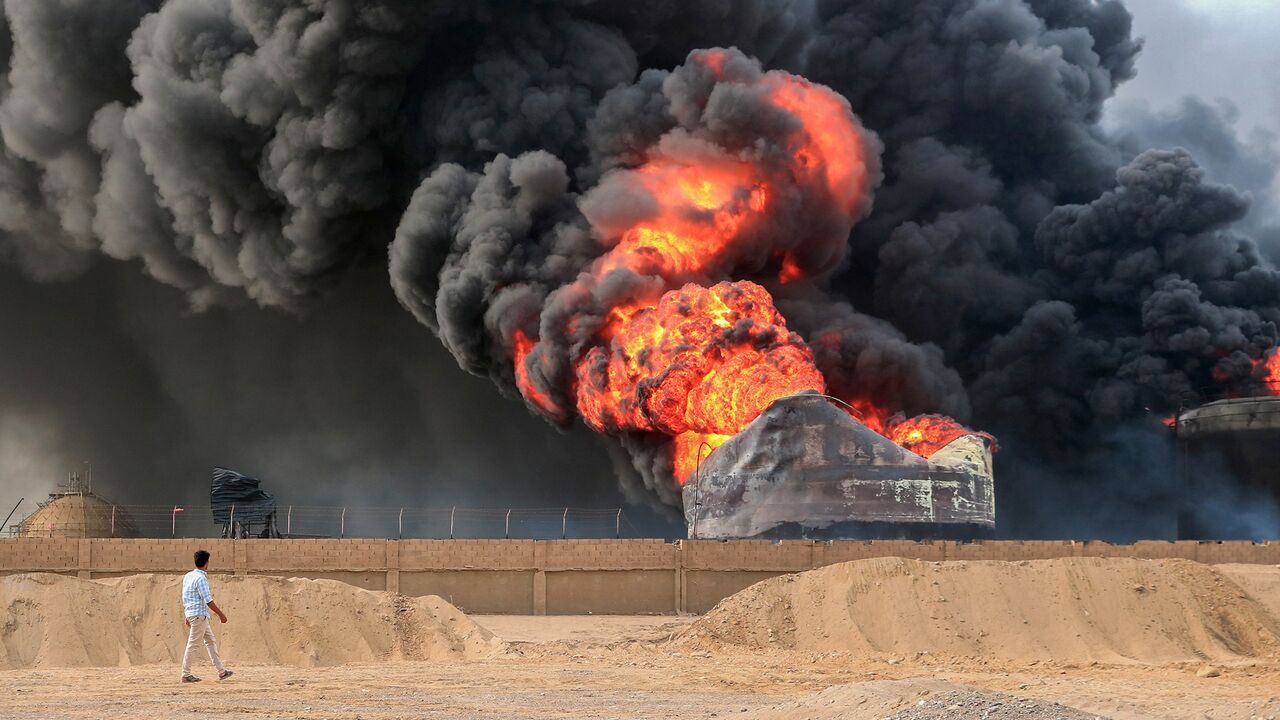 A man walks across from a raging fire at oil storage tanks a day after Israeli strikes on the port of Yemen's Houthi-held city of Hodeidah on July 21, 2024. 