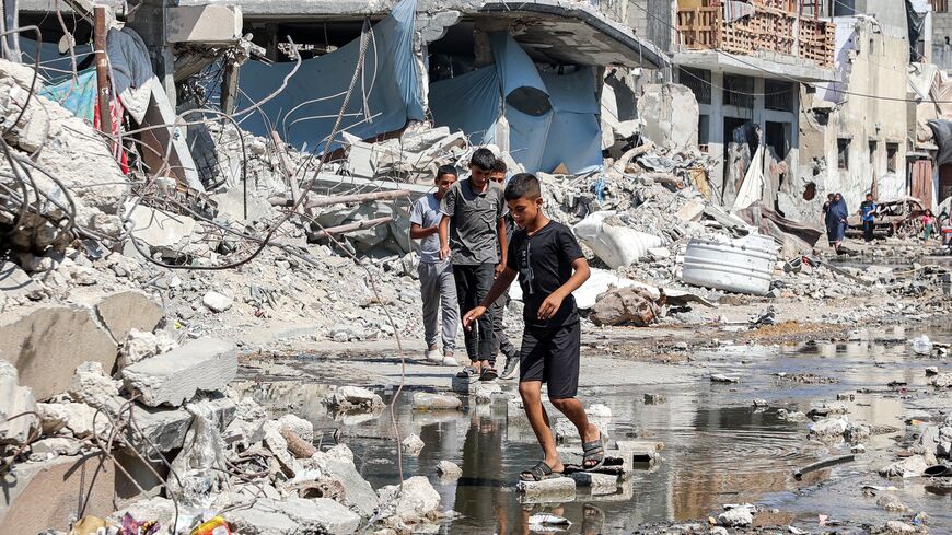 Boys walk on dry bricks to traverse a puddle of sewage water past mounds of trash and rubble along a street in the Jabalia camp for Palestinian refugees, northern Gaza Strip, August 14, 2024.