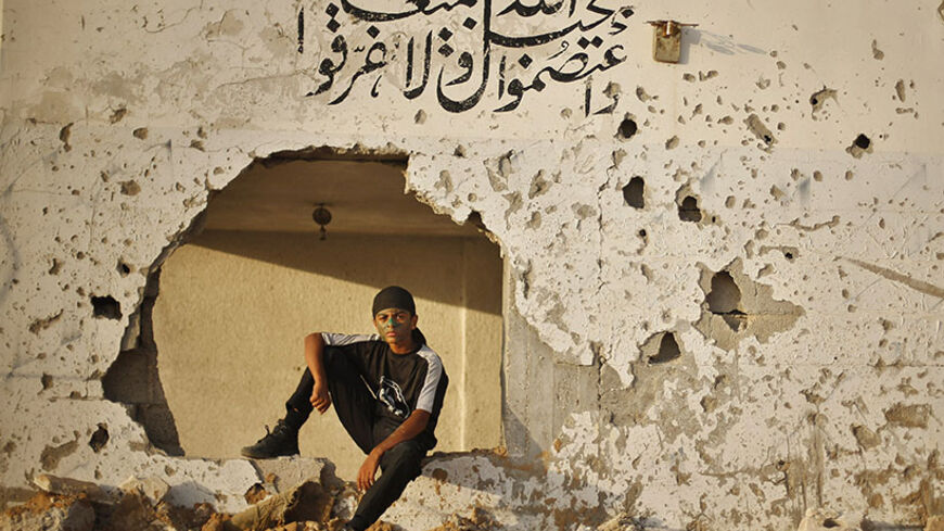 A young Palestinian poses for a photograph after participating in a military-style graduation ceremony at Fajer Al-Entesar (dawn of victory) summer camp, organised by the Hamas movement, in Gaza City June 19, 2014. Hamas stages dozens of military-style summer camps for young Palestinians in the Gaza Strip to prepare them to "confront any possible Israeli attack", organisers said. The writing on the wall is a verse from holy Koran that reads: "And hold firmly to the rope of Allah all together and do not beco